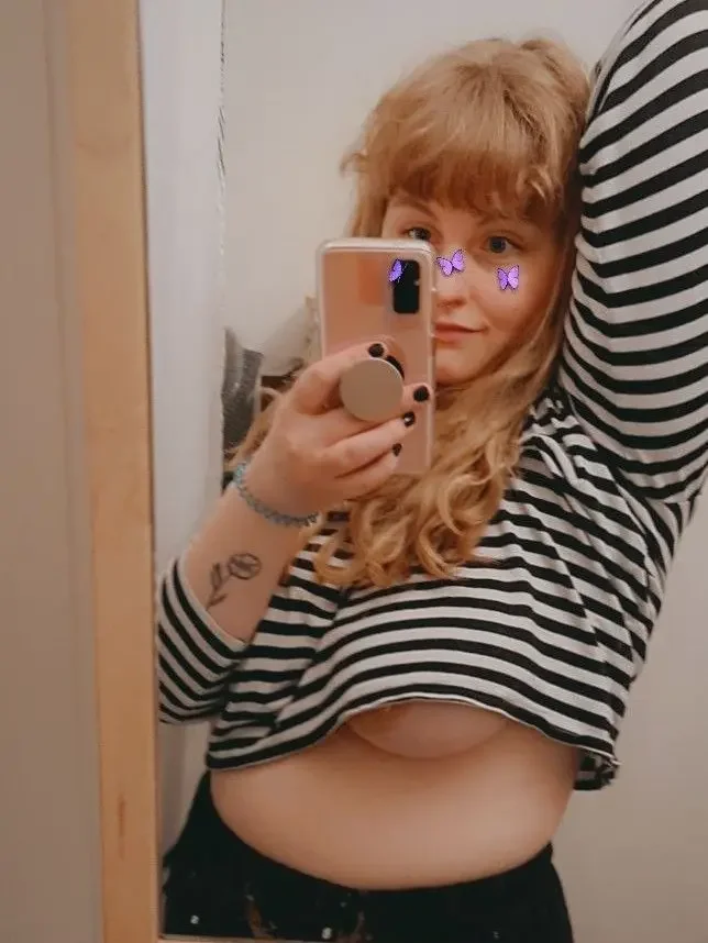 1girl, female only, white female, breasts, long hair, indoors, female, medium hair, standing, medium breasts, selfie, solo, blonde hair, partially dressed, tattoo, no bra, wavy hair, mirror, jewelry, long sleeves, large breasts, shirt, holding, phone, bracelet, holding phone, underboob, black nails, reflection, crop top, striped, striped shirt