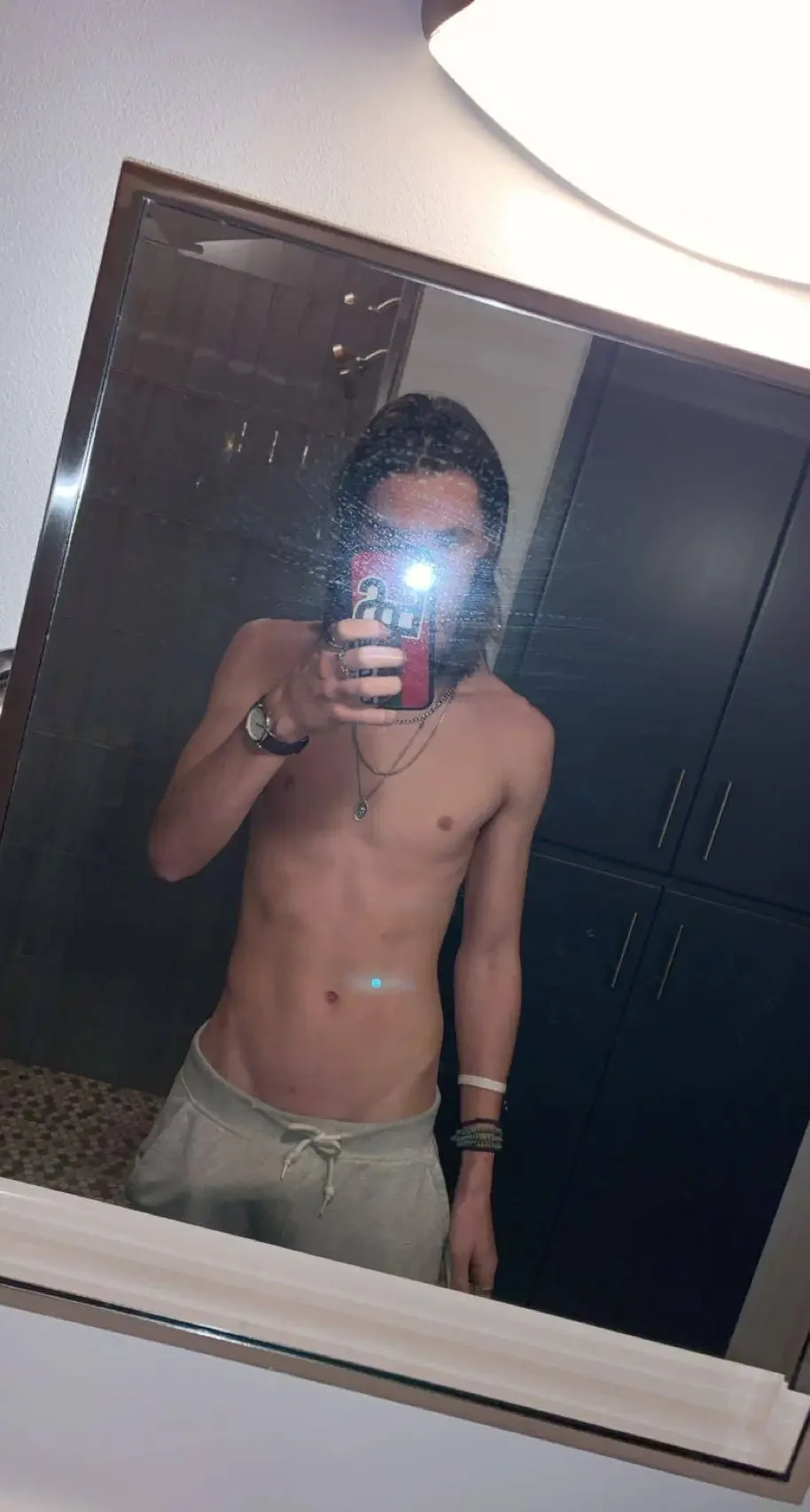 nipples, indoors, medium hair, navel, standing, selfie, black hair, solo, partially dressed, male, male only, 1boy, male focus, white male, necklace, bathroom, mirror, jewelry, pants, holding, bracelet, holding phone, smartphone, topless male
