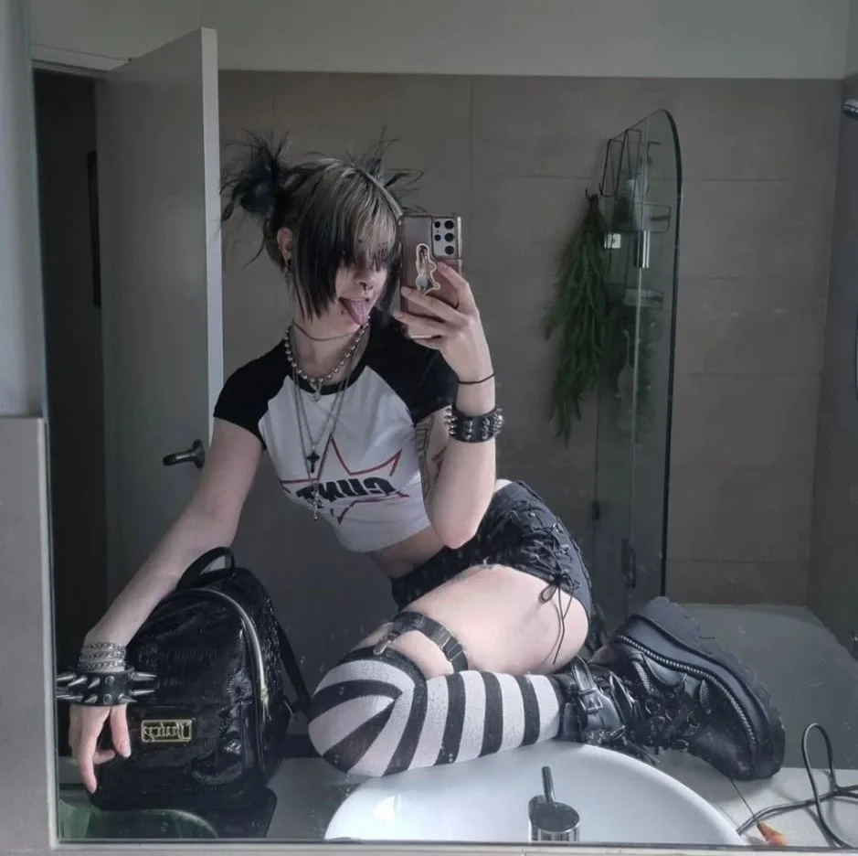 bunni brain, 1girl, female only, white female, caucasian female, light-skinned female, makeup, selfie, standing, blonde hair, piercing, pale-skinned female, black hair, stomach, tattoos, fringe, dyed hair, bangs, thighhighs, non-nude, nose piercing, legwear, mirror selfie, tongue out, bathroom, goth, ear piercing, alt girl, septum piercing, lip piercing, short sleeves, cross necklace, white hair, goth girl, shorts, thigh strap, boots, striped legwear, striped thighhighs, black boots, black shorts, spiked wristband