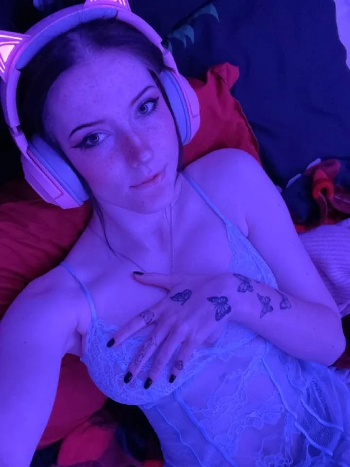 sakurasakelovey, 1girl, female only, white female, looking at viewer, caucasian female, light-skinned female, indoors, front view, makeup, on bed, selfie, black hair, pale-skinned female, bedroom, tattoos, dark hair, non-nude, smile, no bra, lying on bed, sleeveless, headphones, black fingernails, pink headphones, nightgown